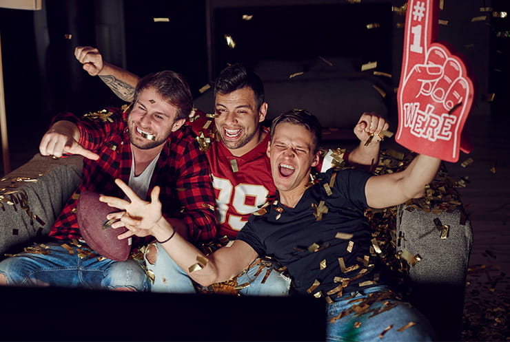 Sports fans celebrating while watching a game on the sofa.